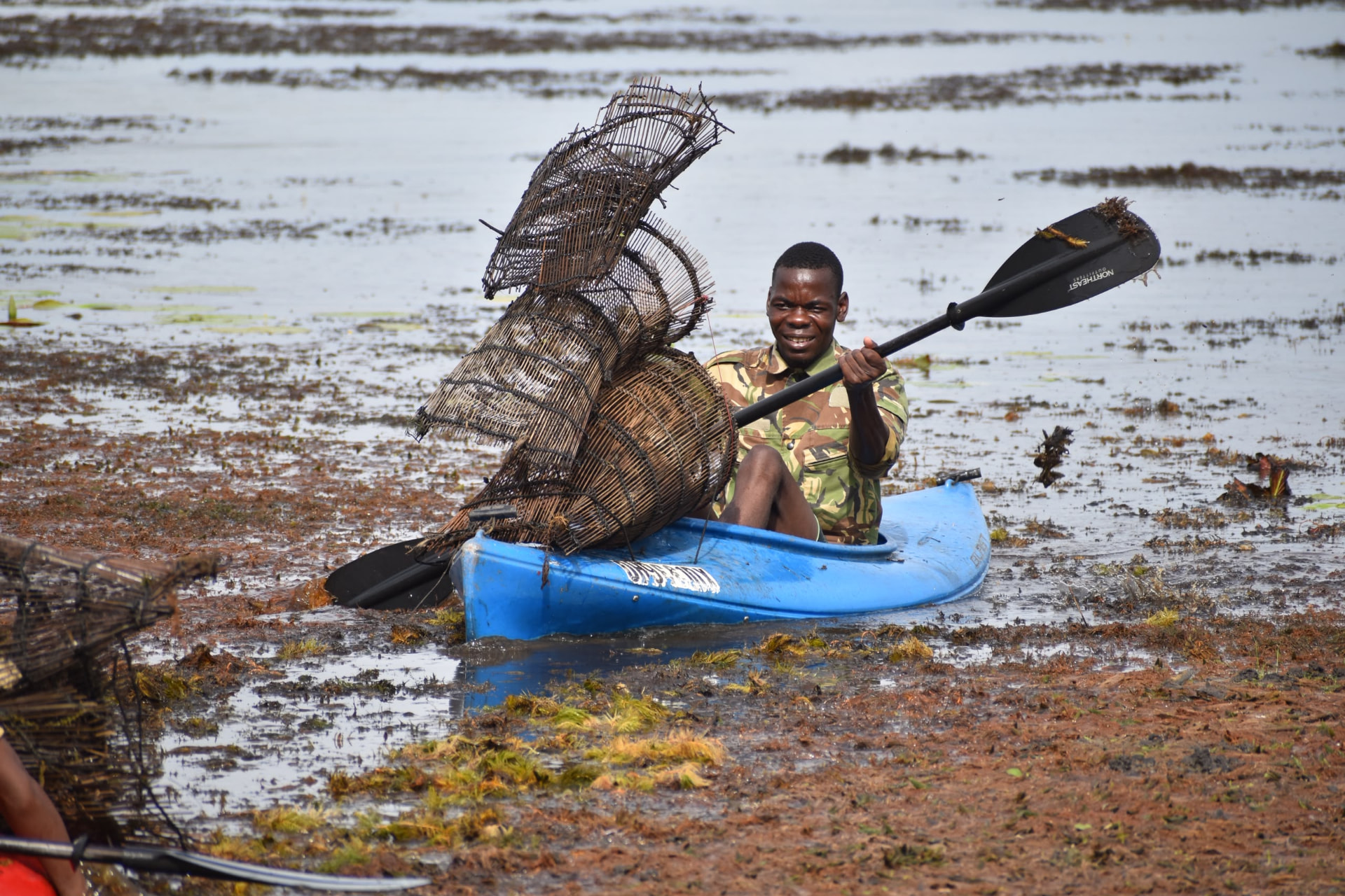 Fisherman paddling a kayak loaded with traditional woven fish traps