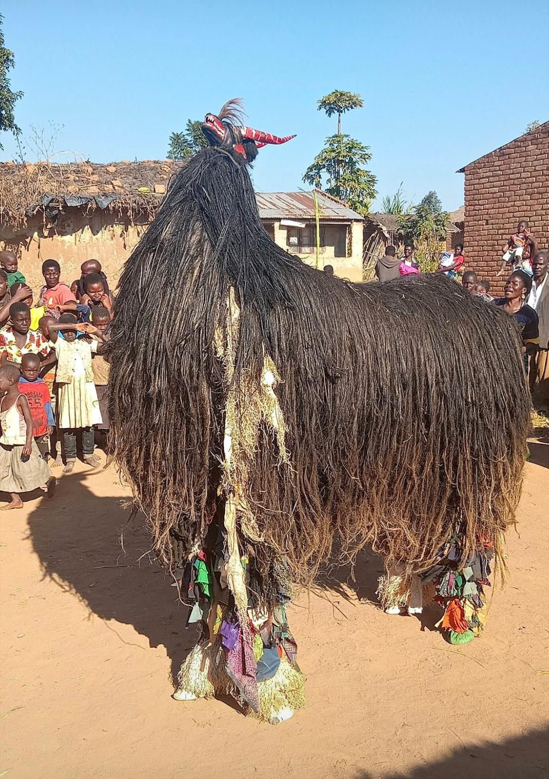 Towering Gule Wamkulu masked figure dancing in a Chewa village
