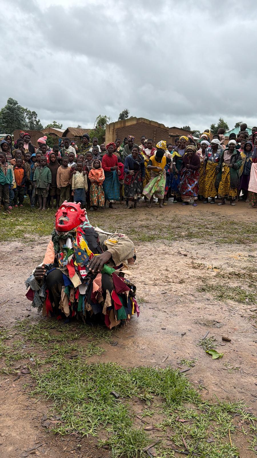 Red-masked Gule Wamkulu dancer kneeling before villagers