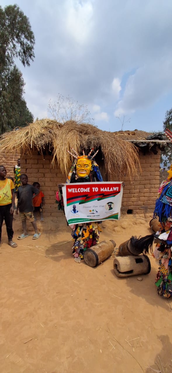 Gule Wamkulu masked dancer holding a welcome banner in a Chewa village