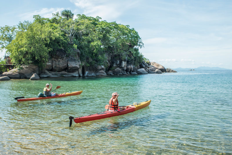 Two guests kayaking on turquoise water beside a rocky island